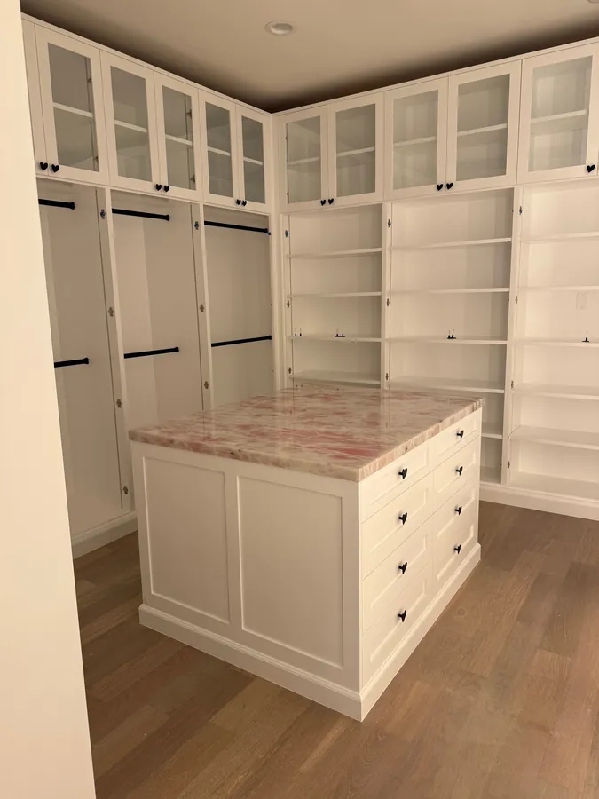White walk-in closet with a center island, glass-front upper cabinets, hanging sections and shelving