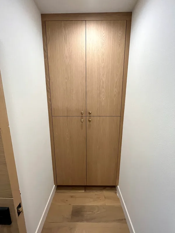 Tall rift-cut oak wardrobe with four flush doors at the end of a white hallway, Los Angeles