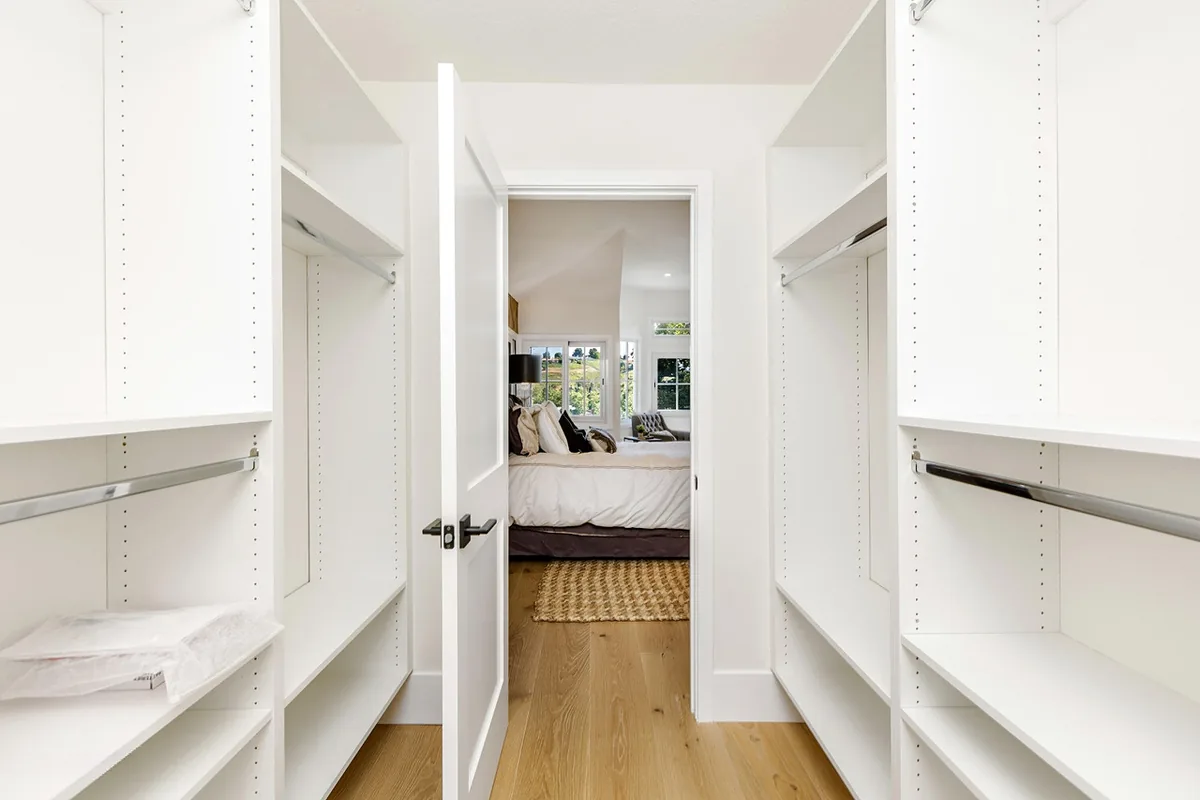 White walk-in closet with hanging and shelving on both sides and an open door at the end